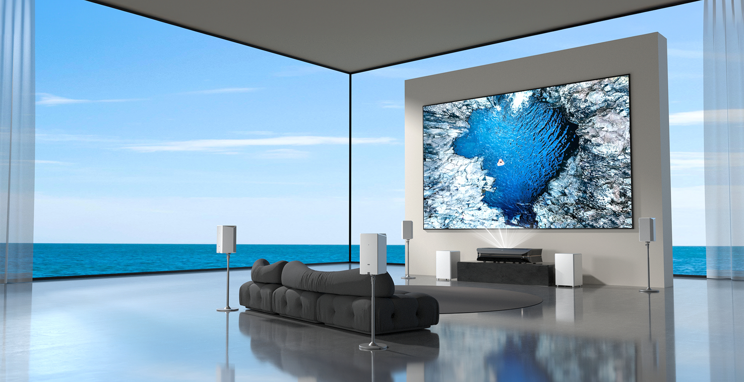 A luxurious, minimalist living room with sea view. It features a large screen illuminated by visible light from an ultra-short-throw projector, plus a white surround sound system.
